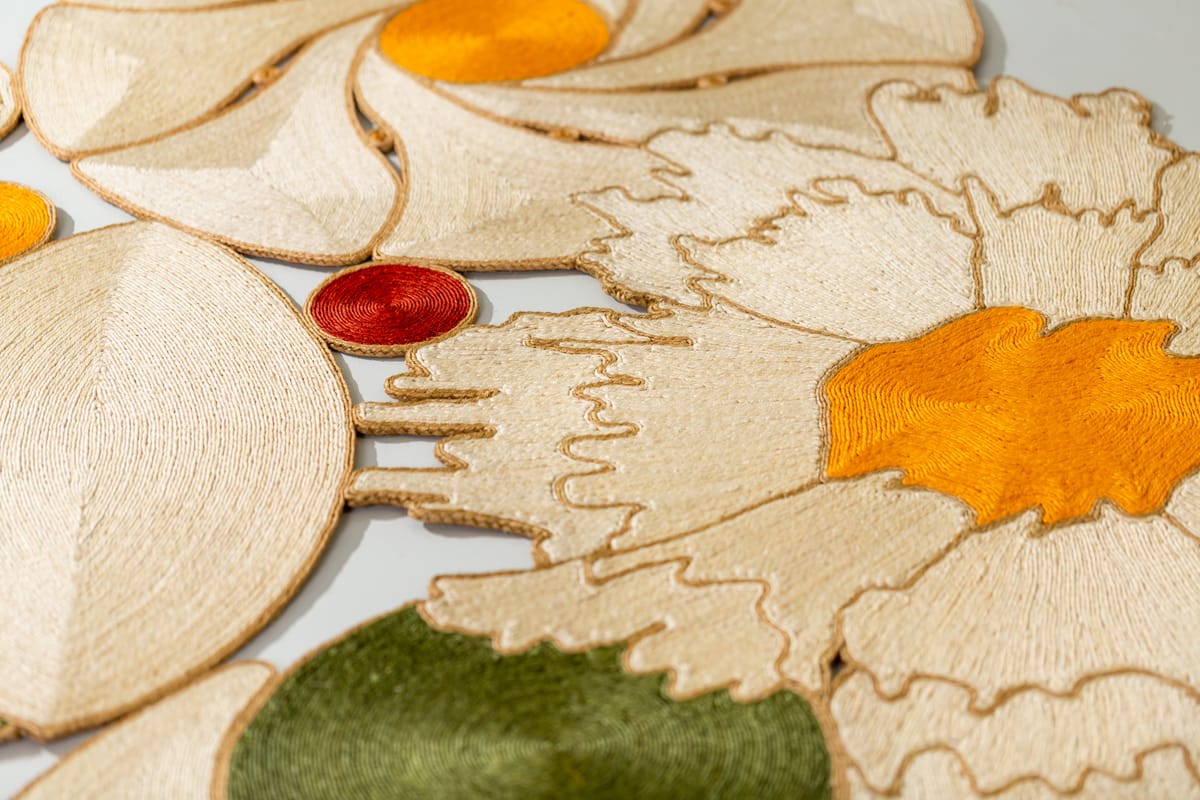 Close view of cream, orange, red, and olive-green sisal textile pieces, coiled in spiral forms, on a light grey background